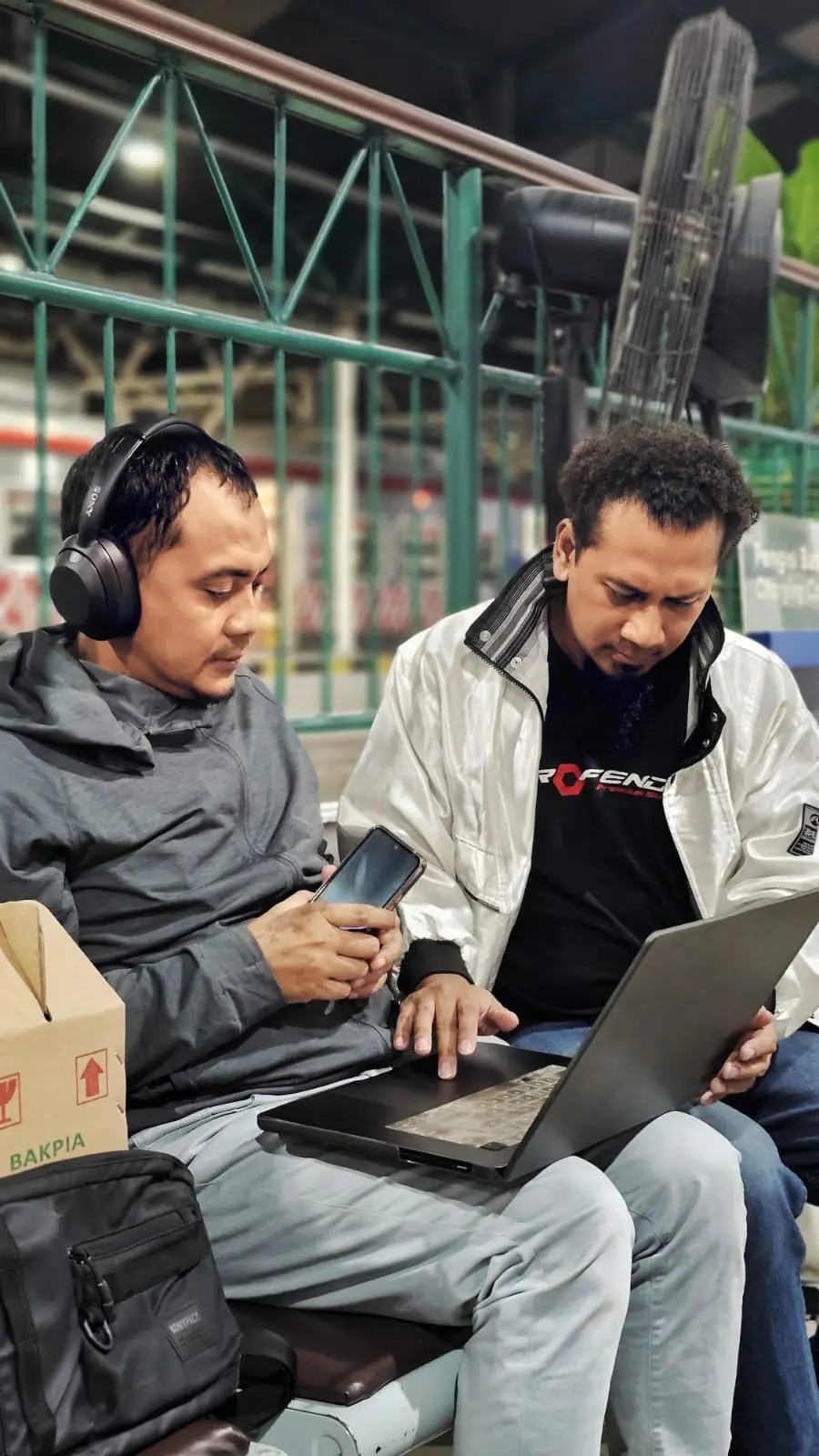 Dua anggota tim memantau rekaman lewat ponsel dan laptop di lokasi produksi.